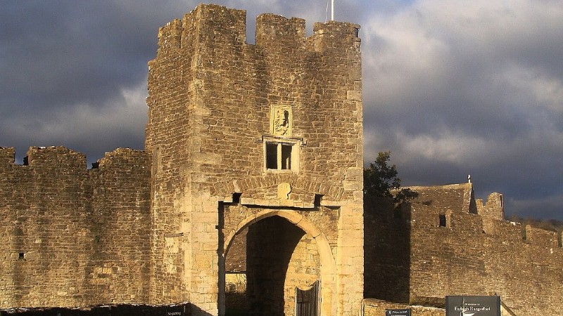 The front gatehouse and walls of a medieval castle, Farleigh Hungerford Castle, on a cloudy day.
